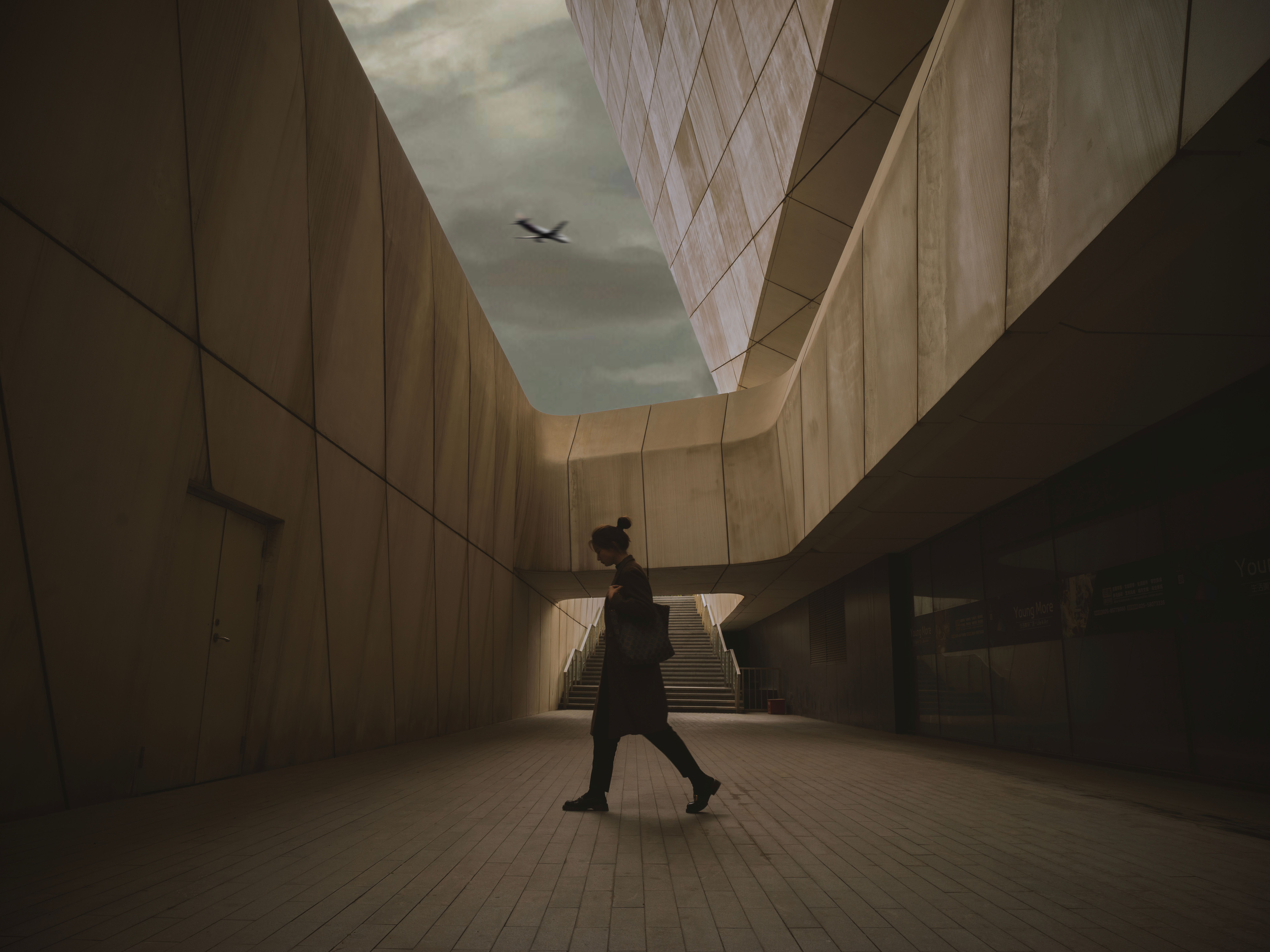 Silhouetted woman walks under modern architecture as airplane flies overhead.