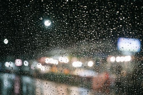 Free Blurred city lights through rain-speckled window at night. Urban ambiance with bokeh effect. Stock Photo
