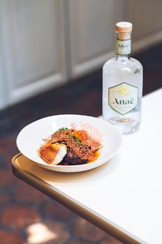 A gourmet dish served alongside a gin bottle on an elegant table setting.