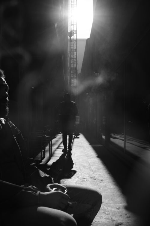 Free Dramatic black and white urban scene with silhouetted figures in a narrow alley, showcasing strong light and shadow contrasts. Stock Photo