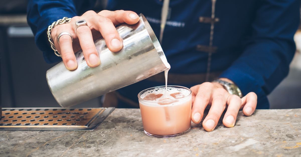 Professional bartender pouring a fresh cocktail into a glass at a bar counter.