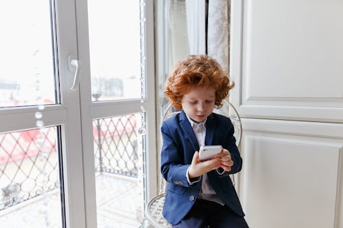 赤毛の小さな少年は、自宅の部屋に座ってスマートフォンを使用しています
