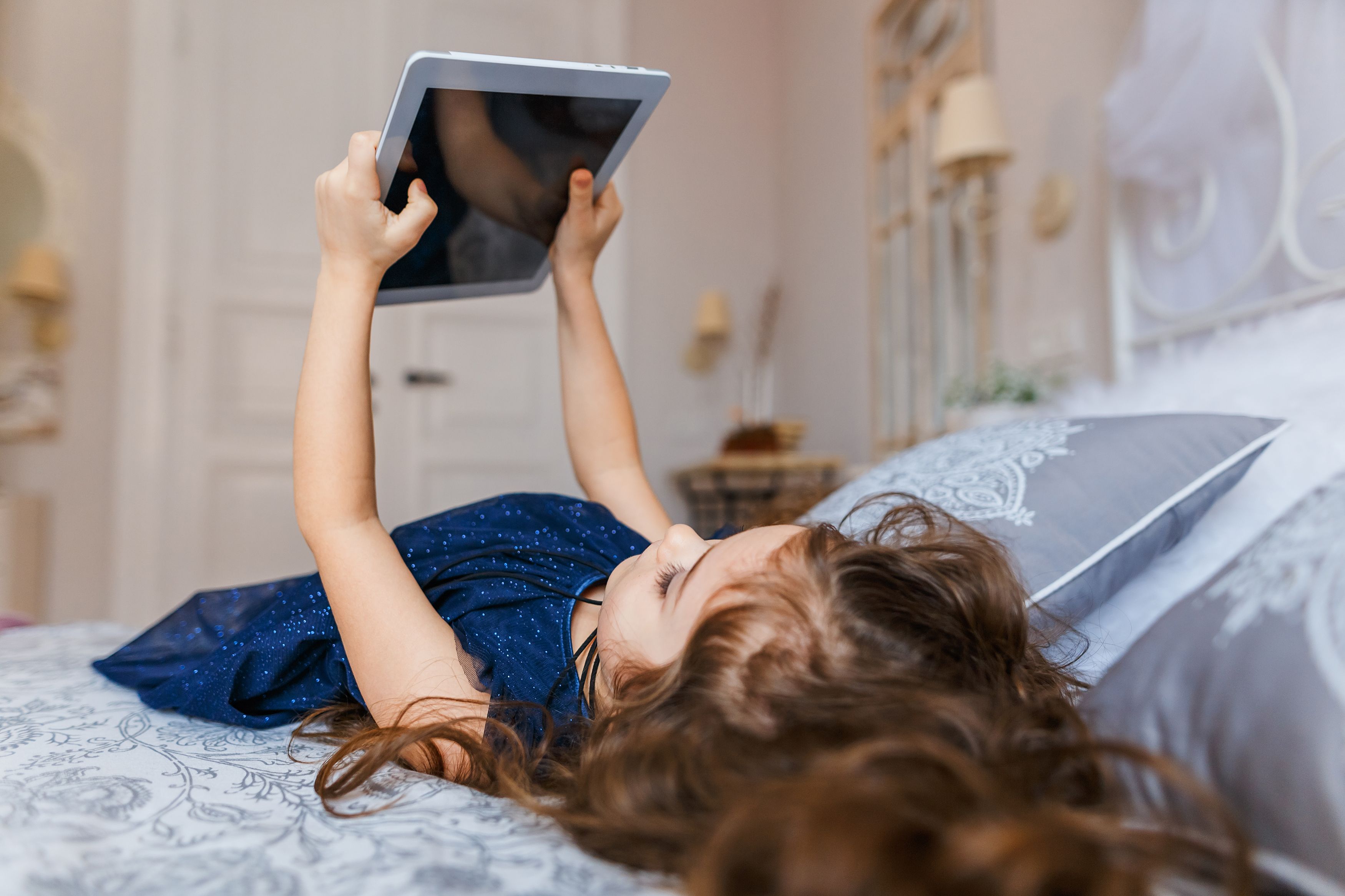 Cute little girl with curly hair using digital tablet while lying in ...