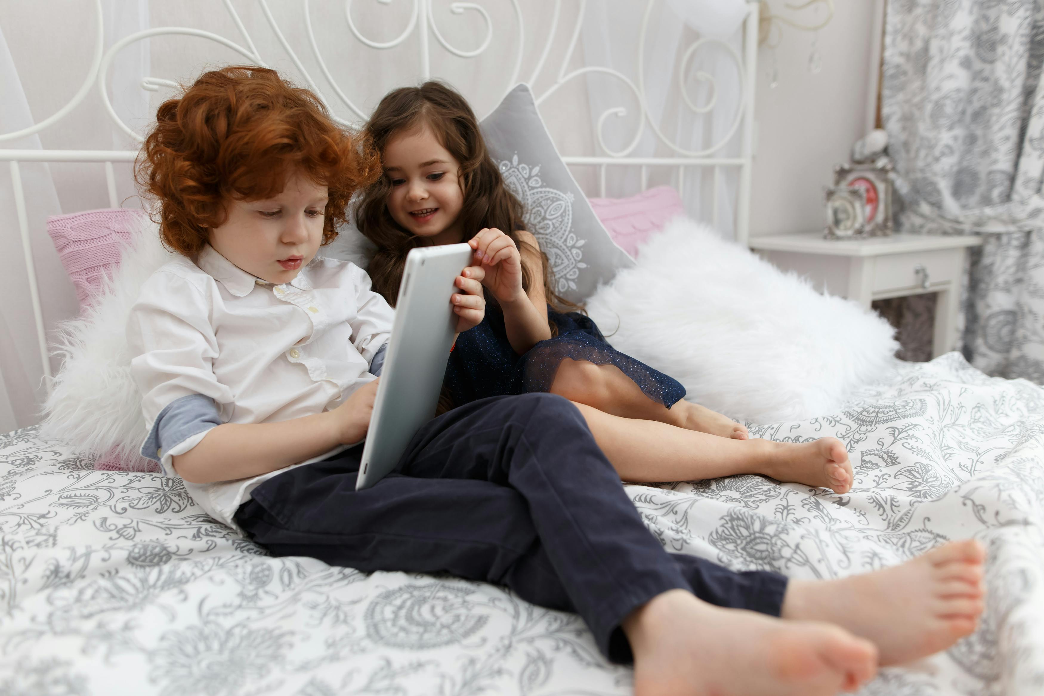 a boy and a girl lie on the bed and play with a tablet computer