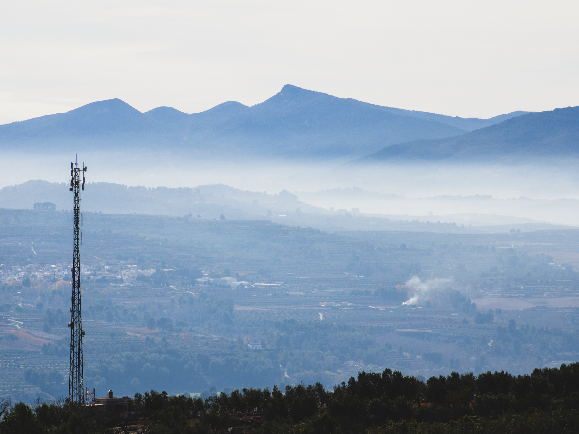 Serene rural landscape with a radio mast and misty mountains in the background.