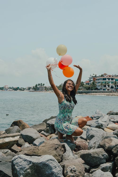 Free Woman Sitting While Holding Balloons Near Body of Water Stock Photo