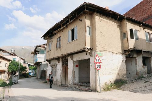 Free A man walks past a damaged building on a sunny urban street corner. Stock Photo