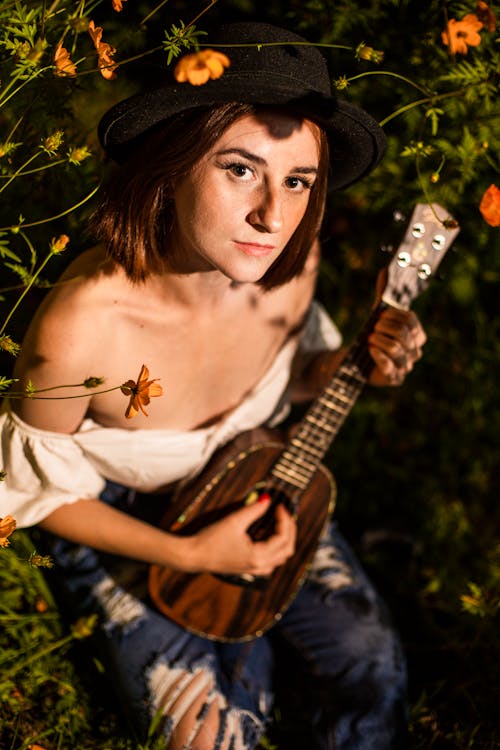 Woman in Hat Sitting with Musical Instrument among Flowers