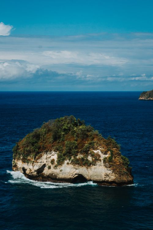 Free A small island with lush greenery surrounded by the deep blue ocean under a clear sky. Stock Photo
