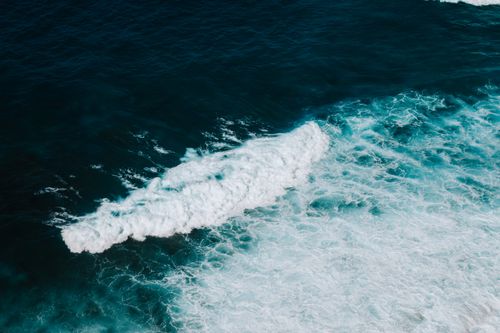 Free Aerial view of ocean waves creating white foam as they crash on the shore. Stock Photo