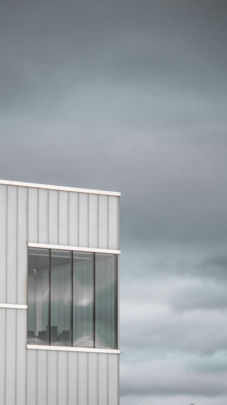 Sleek urban building corner with large windows under a cloudy sky, showcasing modern architecture.
