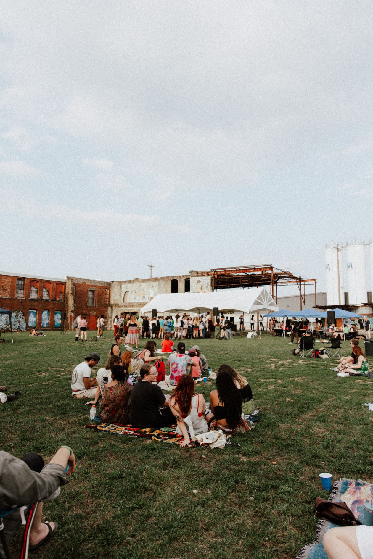 People sitting on the grass at an outdoor festival enjoying live music in a sunny urban park setting