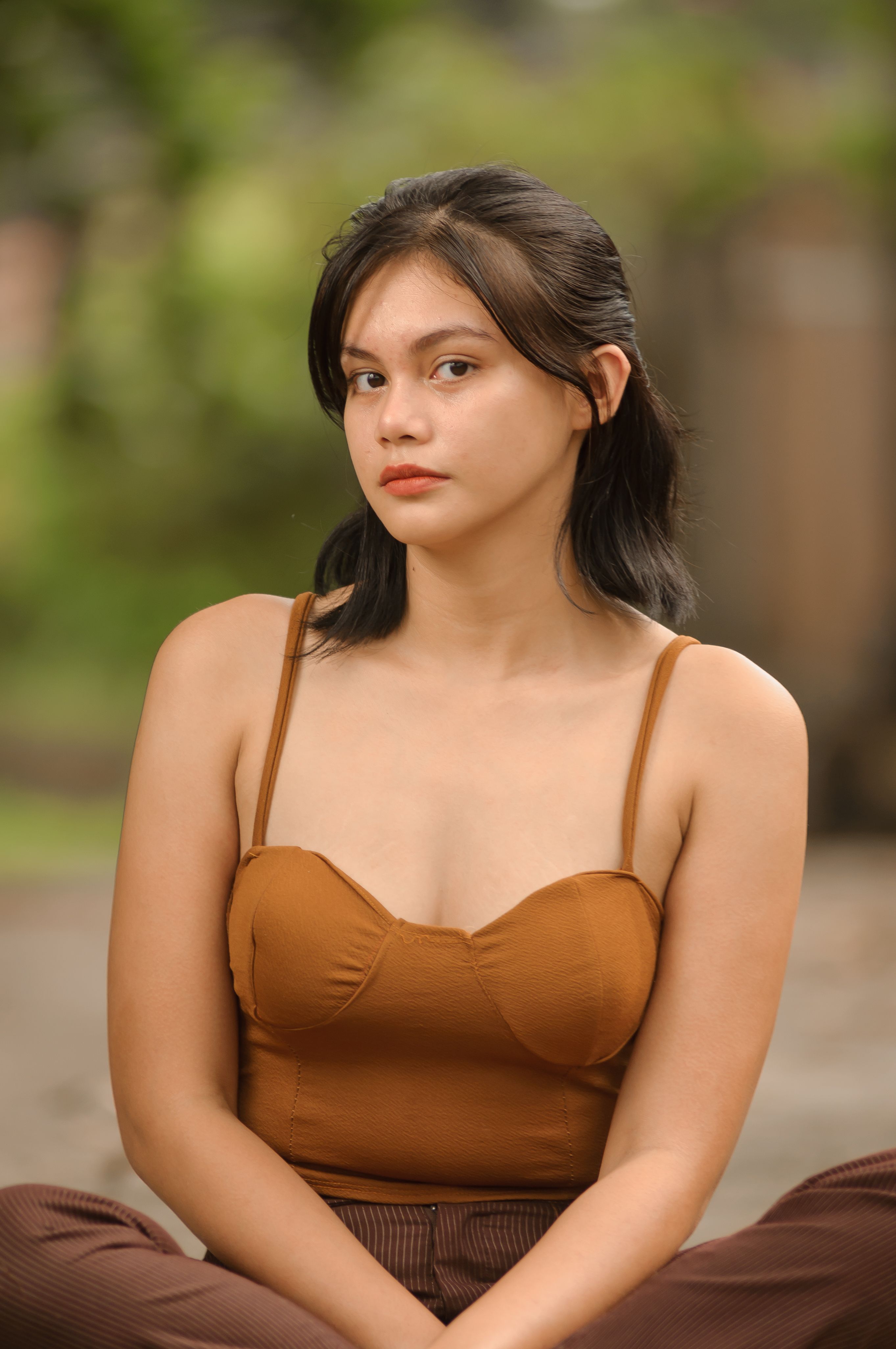 Portrait of a young Asian woman sitting outdoors in casual fashion attire.