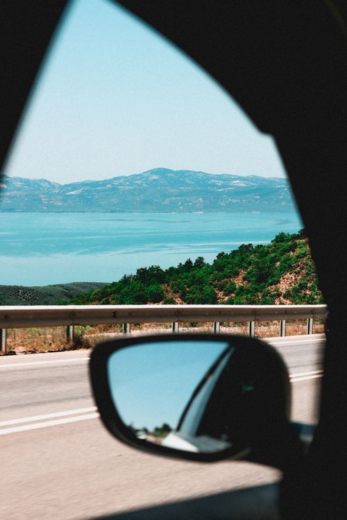 Free View of mountains and lake through a car window, capturing travel excitement. Stock Photo
