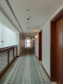 A well-lit hotel corridor featuring wooden doors and elegant carpet, showcasing modern interior design.