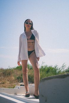 Woman posing in black bikini with white shirt on a sunny beach day.