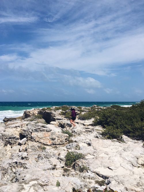 Free Woman walking on rocky coastline of Isla Mujeres under a bright blue sky. Stock Photo