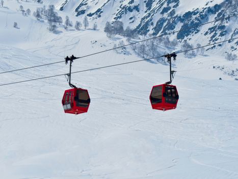 Two red ski lifts traverse a snowy mountain during winter, surrounded by scenic views.