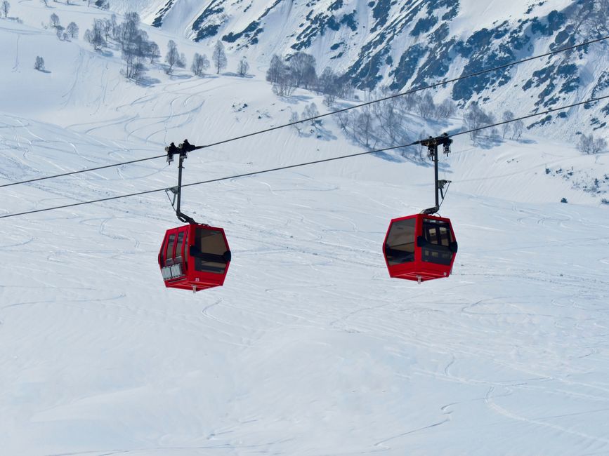 Two red ski lifts traverse a snowy mountain during winter, surrounded by scenic views.