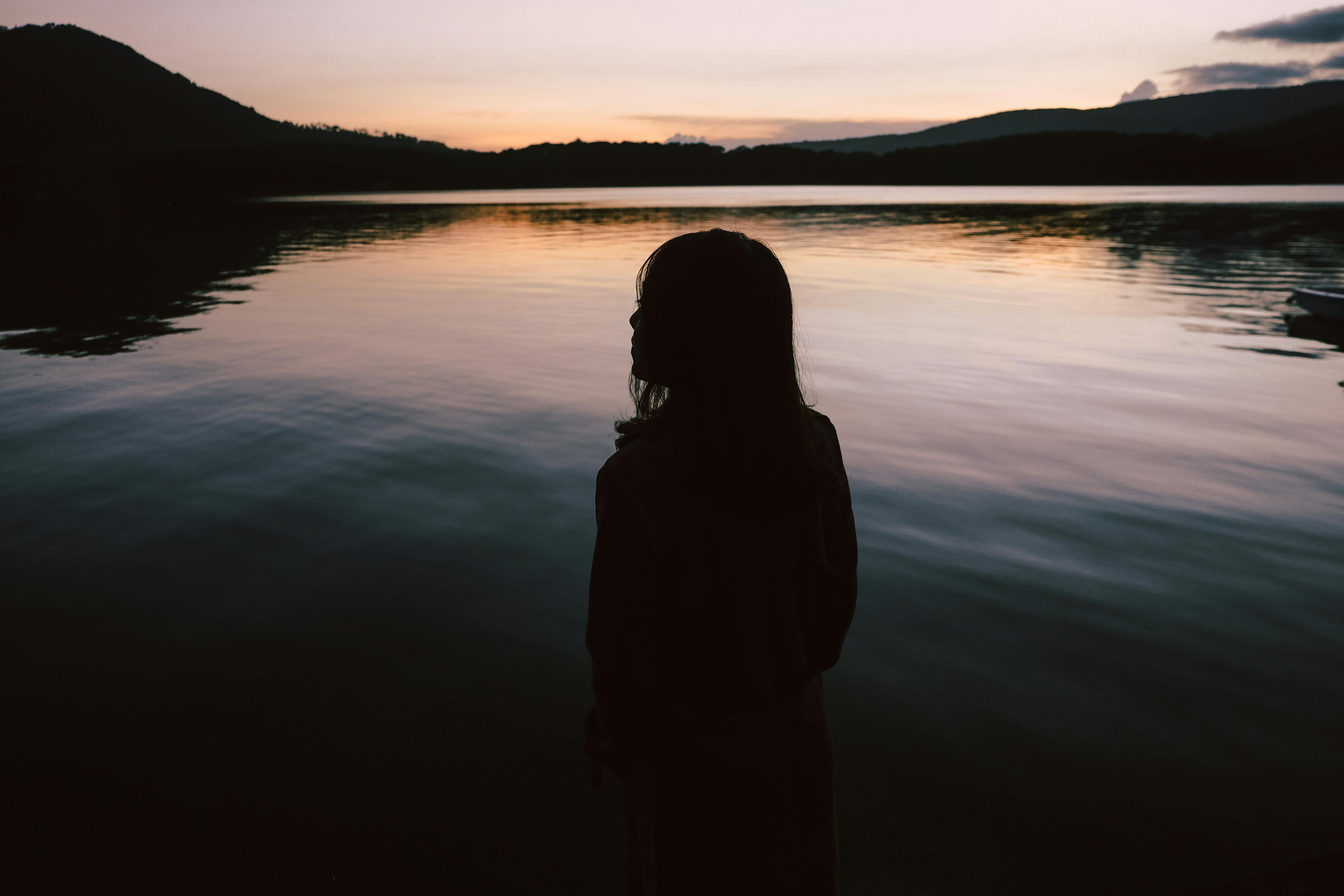 Silhouette Of Woman Standing Near Body Of Water · Free Stock Photo