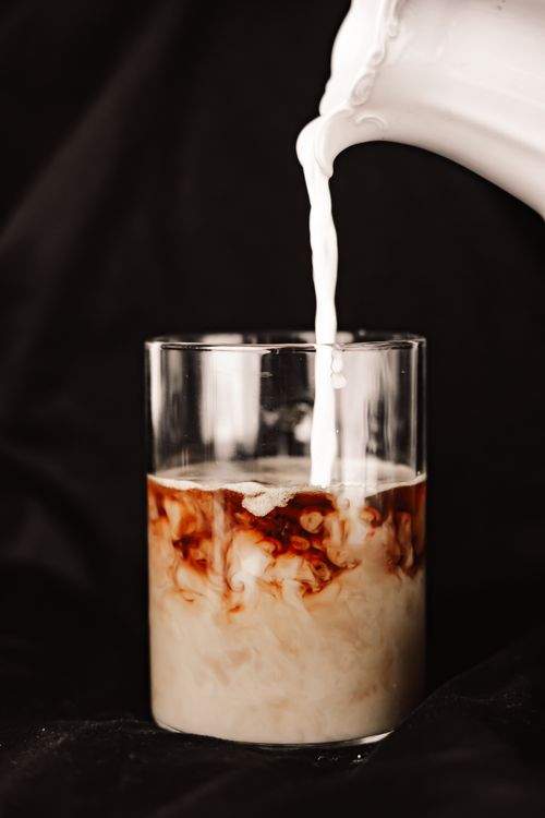 Free Close-up of milk being poured into iced coffee, blending beautifully in a clear glass. Stock Photo