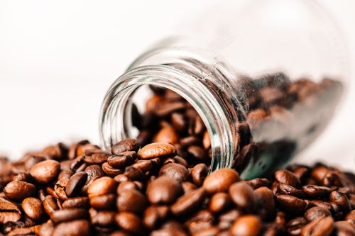 Free Artistic close-up of roasted coffee beans spilling out of a glass jar, showcasing rich, aromatic textures. Stock Photo