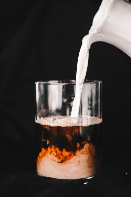 Free Dynamic close-up of milk being poured into black coffee, creating a creamy swirl against a dark background. Stock Photo