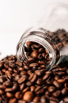 Aromatic coffee beans spilling from a glass jar, perfect for a cafe theme.