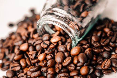 Free A detailed shot of aromatic coffee beans spilling from a transparent glass jar onto a surface. Stock Photo