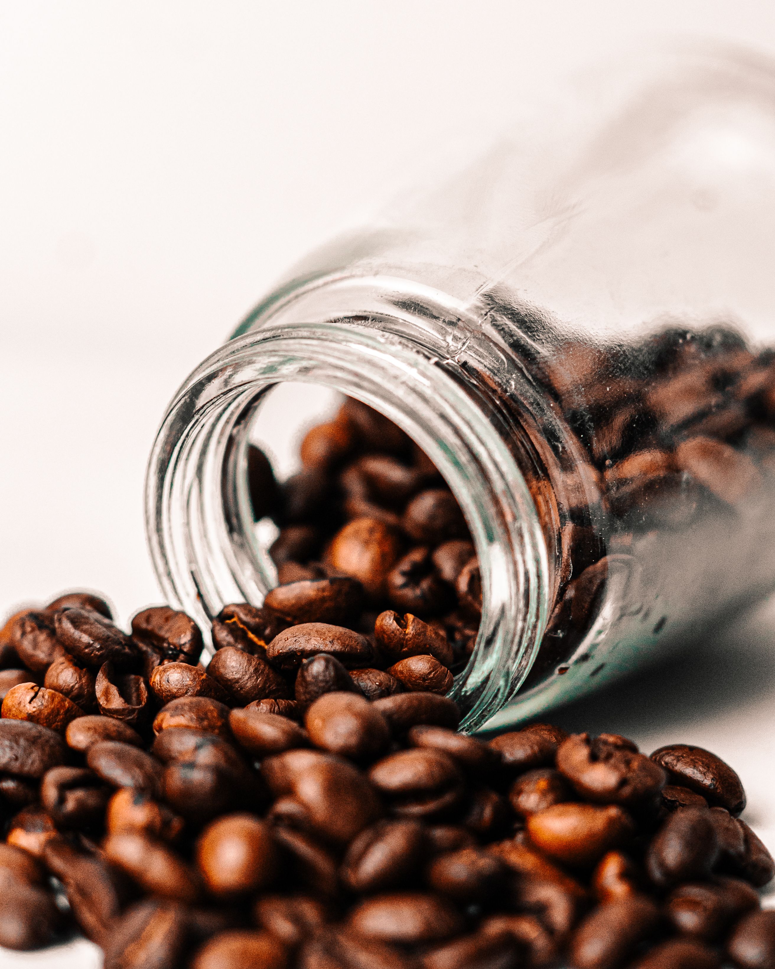 close-up of aromatic coffee beans spilling from a glass jar showcasing rich brown tones.