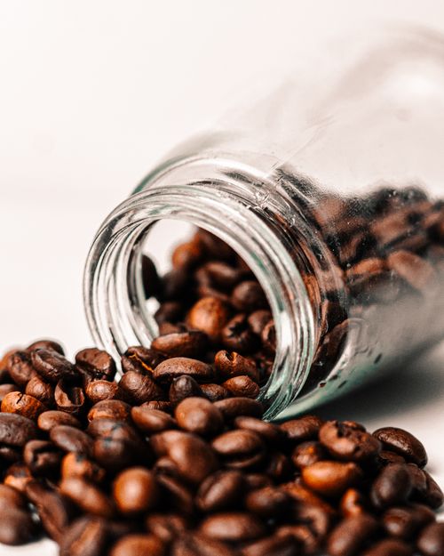 Free Close-up of aromatic coffee beans spilling from a glass jar showcasing rich brown tones. Stock Photo