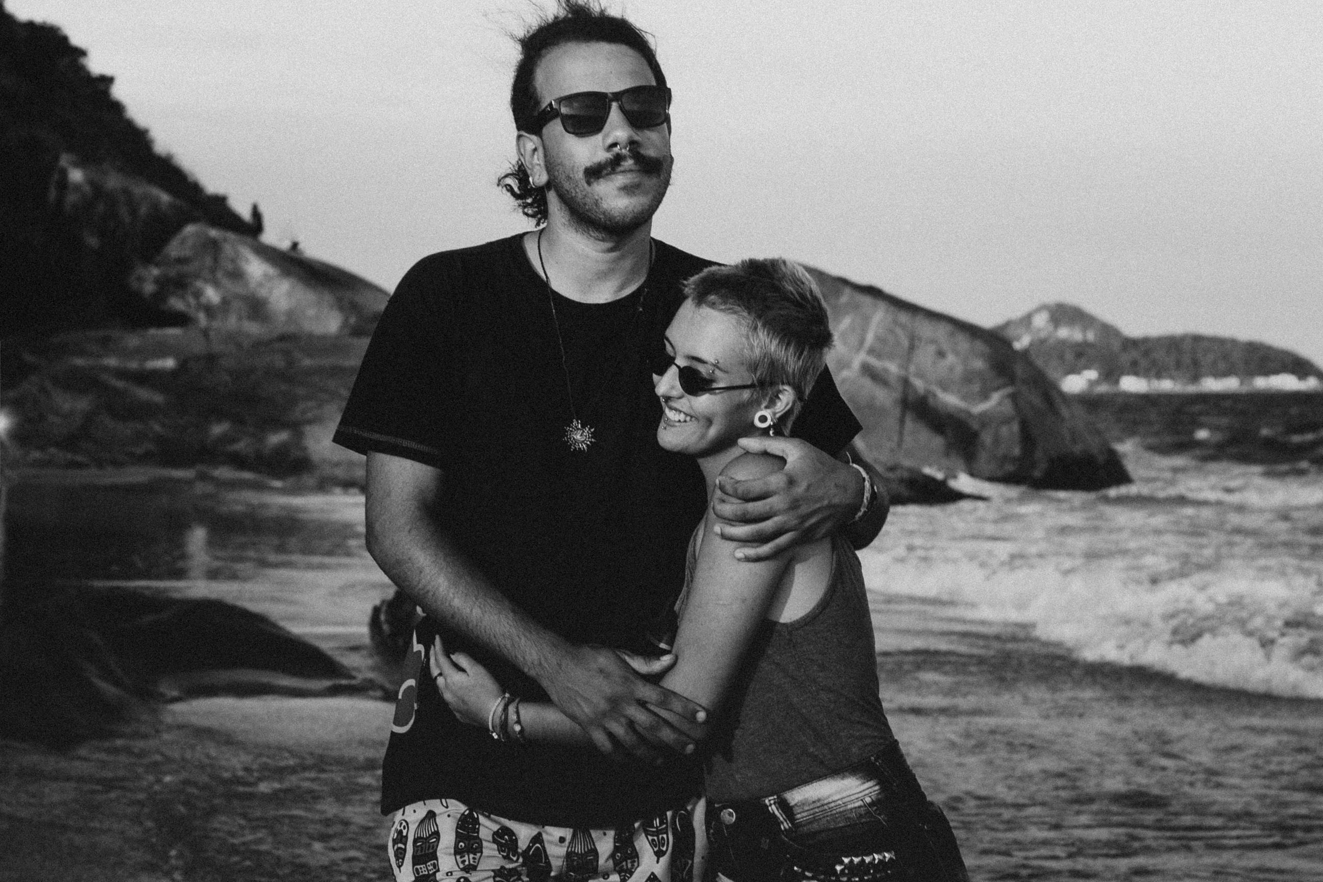 A couple embracing on a rocky beach, smiling and enjoying a vacation moment.