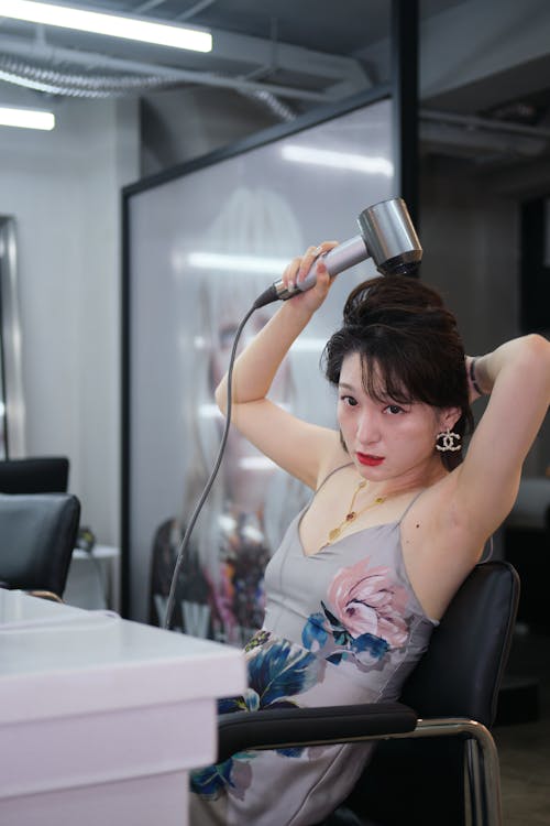 Woman in Dress Sitting on Armchair and Drying Hair