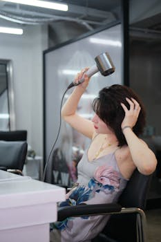 A woman in a floral dress uses a hairdryer at a stylish salon, focused on her styling.