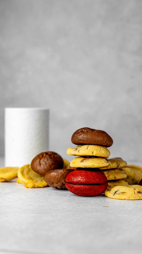 Free Vertical shot of colorful assorted cookies on a gray surface with a white cup in the background. Stock Photo