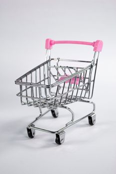 Stylish studio shot of a miniature shopping cart with a pink handle, perfect for retail-themed designs.
