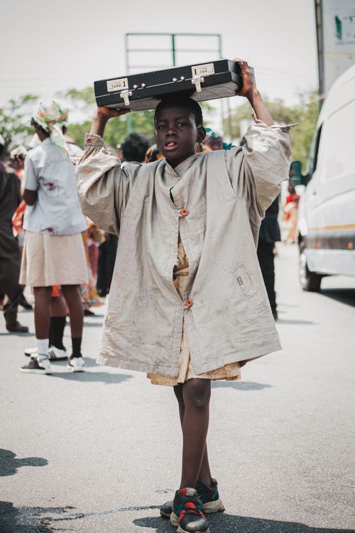 Free A young African boy carries a suitcase on a bustling street in Accra, Ghana. Stock Photo