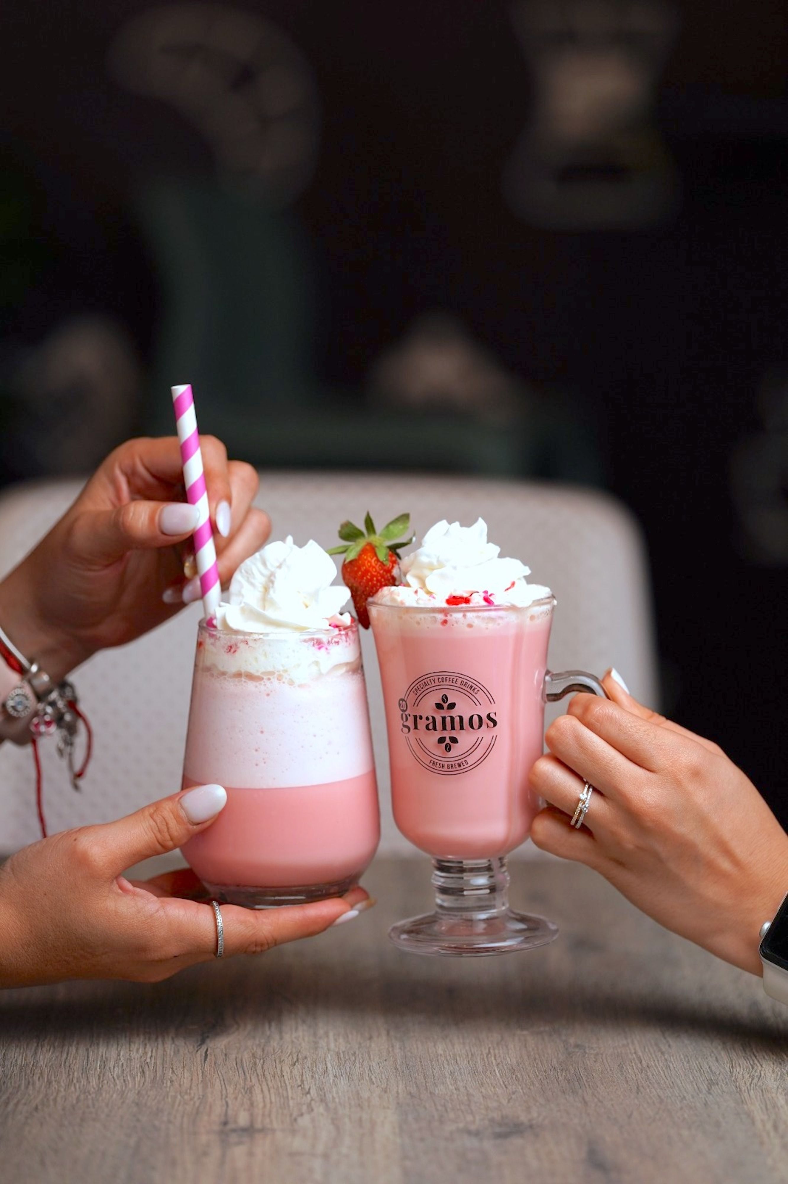 A tall glass of pale pink strawberry milk with sliced fresh strawberries on the rim and a few whole berries scattered beside it on a wooden table.
