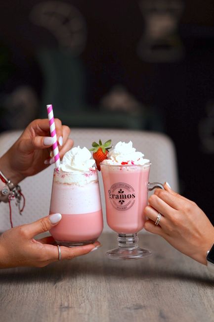 A tall glass of pale pink strawberry milk with sliced fresh strawberries on the rim and a few whole berries scattered beside it on a wooden table.