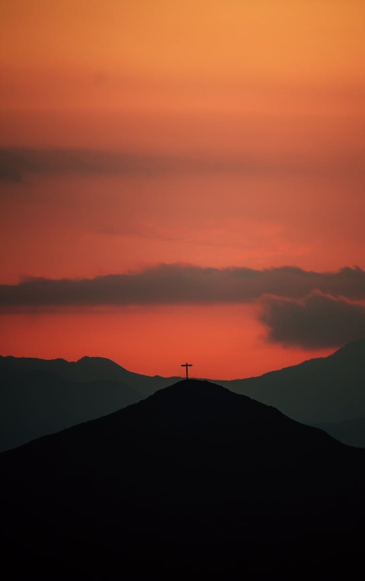 Silhouetted Mountain With A Cross At The Top At Sunset