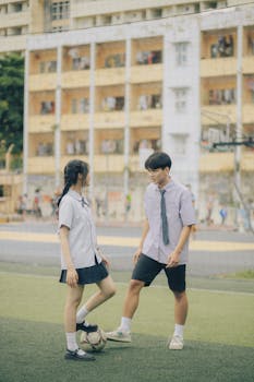 Asian teen couple playing football on a school field, showcasing youthful energy and urban lifestyle.