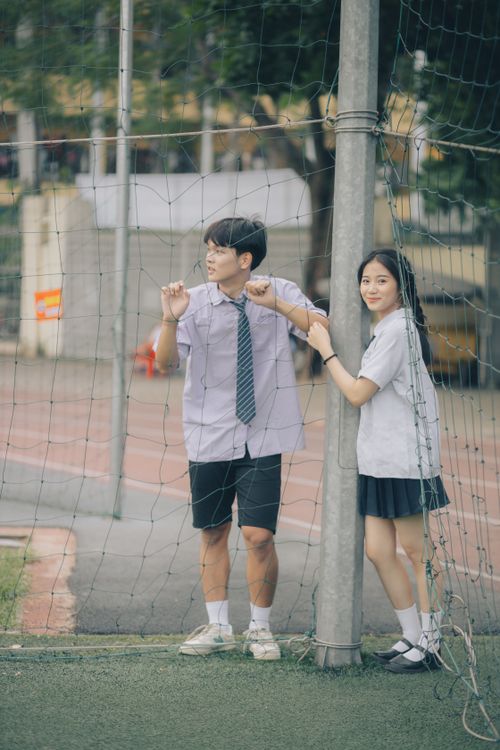 Free Two Asian teenagers in uniform standing by a sports net, smiling outdoors. Stock Photo