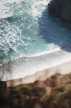 An aerial shot showcasing waves crashing onto a picturesque sandy beach bordered by natural foliage.