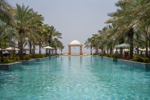 Free A serene luxury resort pool surrounded by palm trees and a central gazebo under a clear sky. Stock Photo