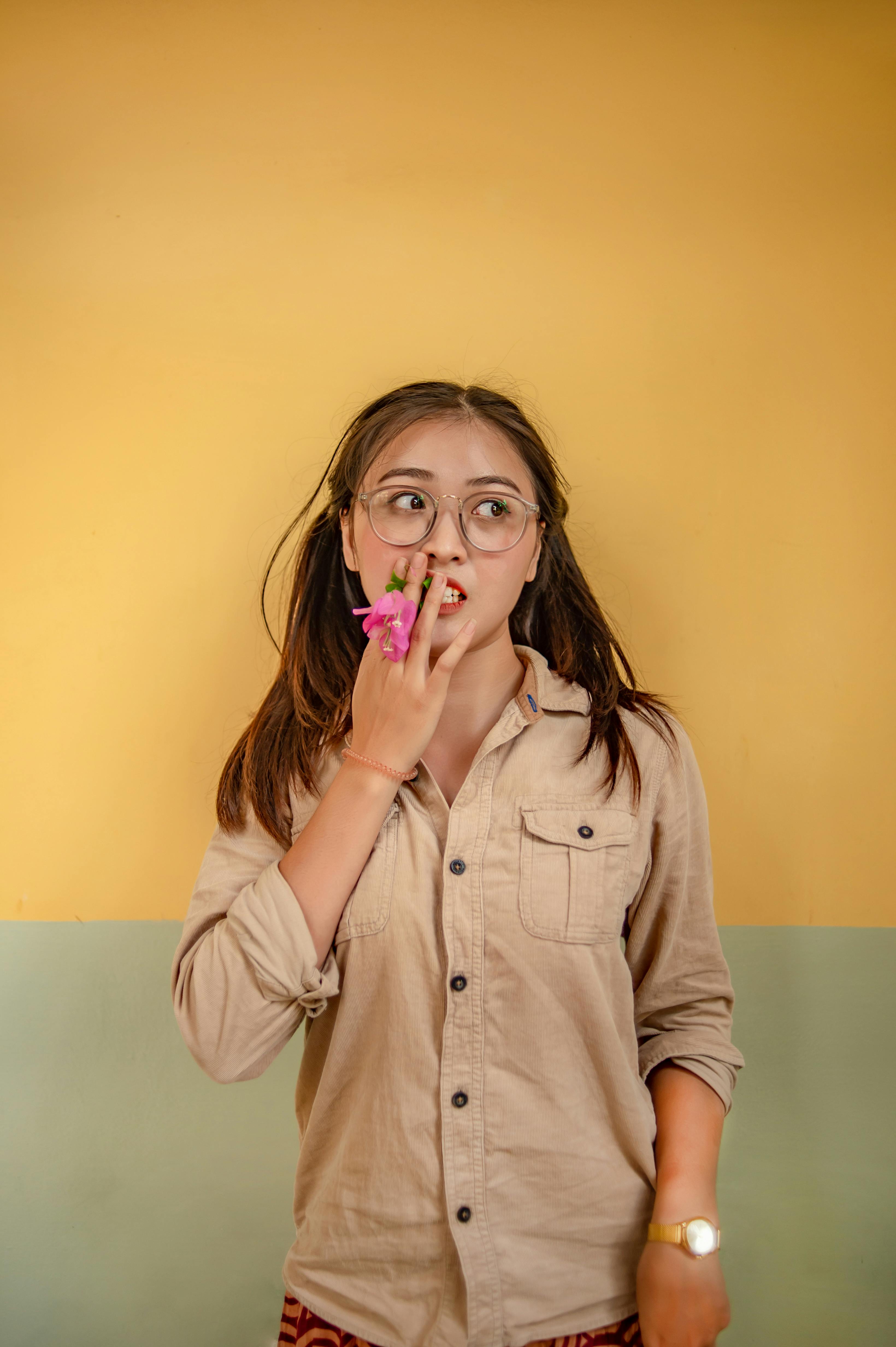 一位戴眼镜的年轻女子在室内靠着一面充满活力的墙壁，手捧鲜花