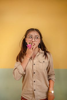 一位戴眼镜的年轻女子在室内靠着一面充满活力的墙壁，手捧鲜花