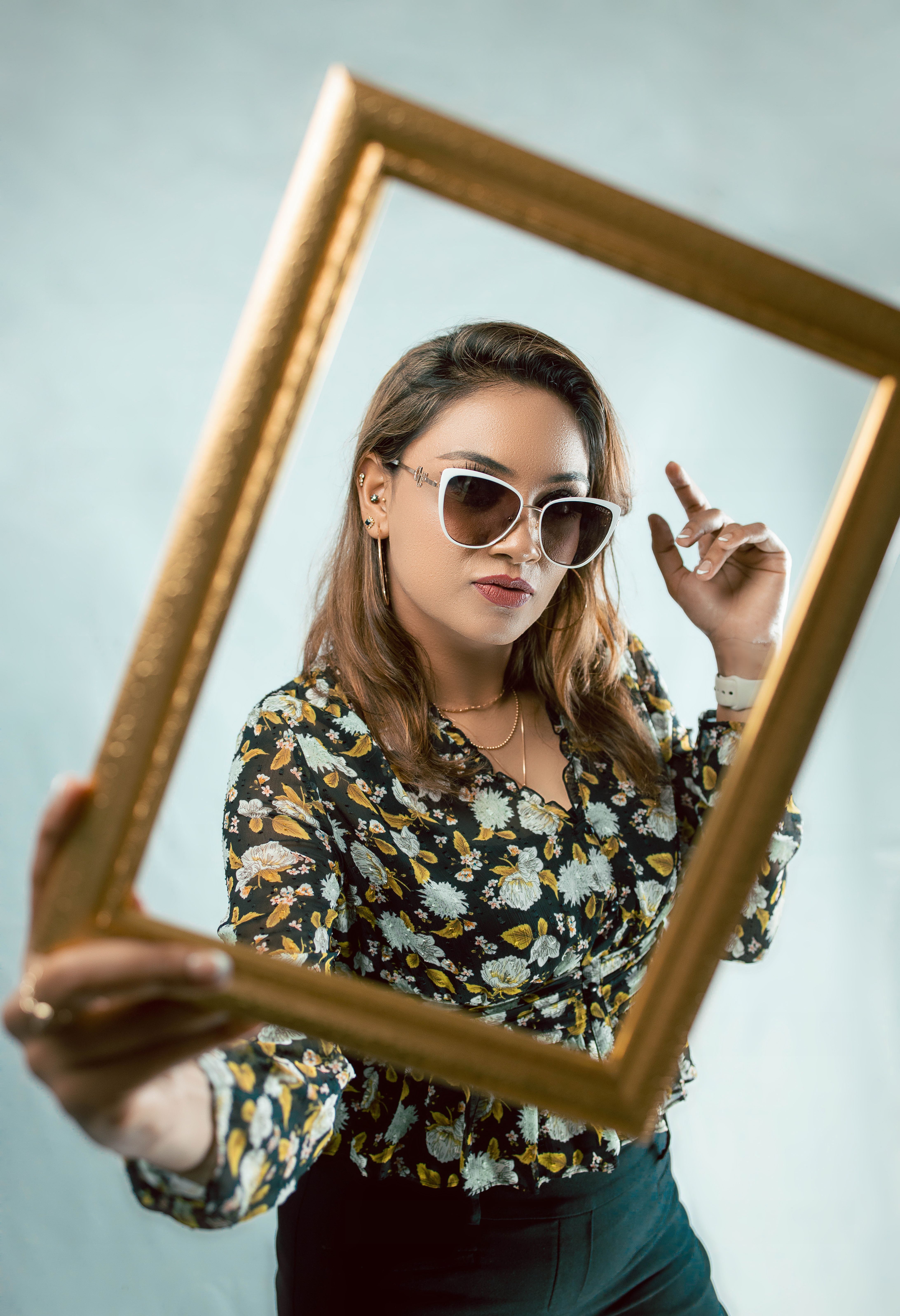 Chic woman with sunglasses holding a frame, showcasing fashion and bold expressions.