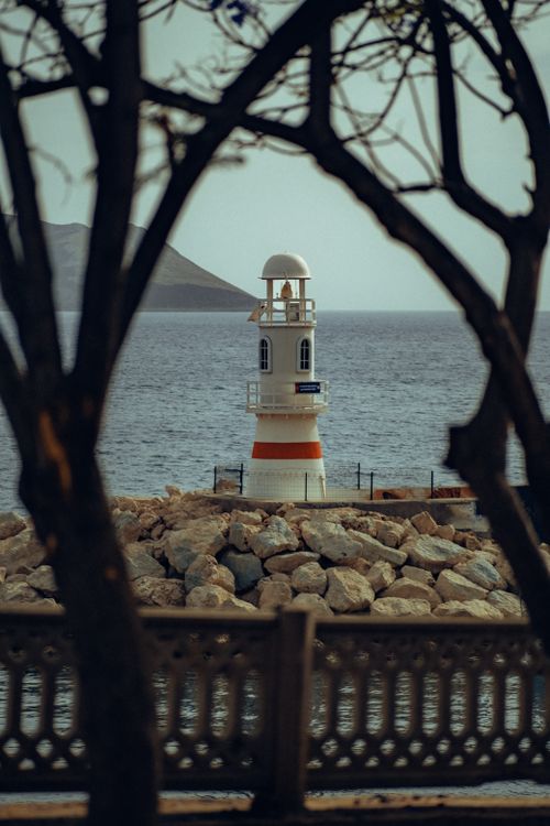 Free Serene view of a lighthouse on rocky shores, framed by trees in Antalya, Türkiye. Stock Photo
