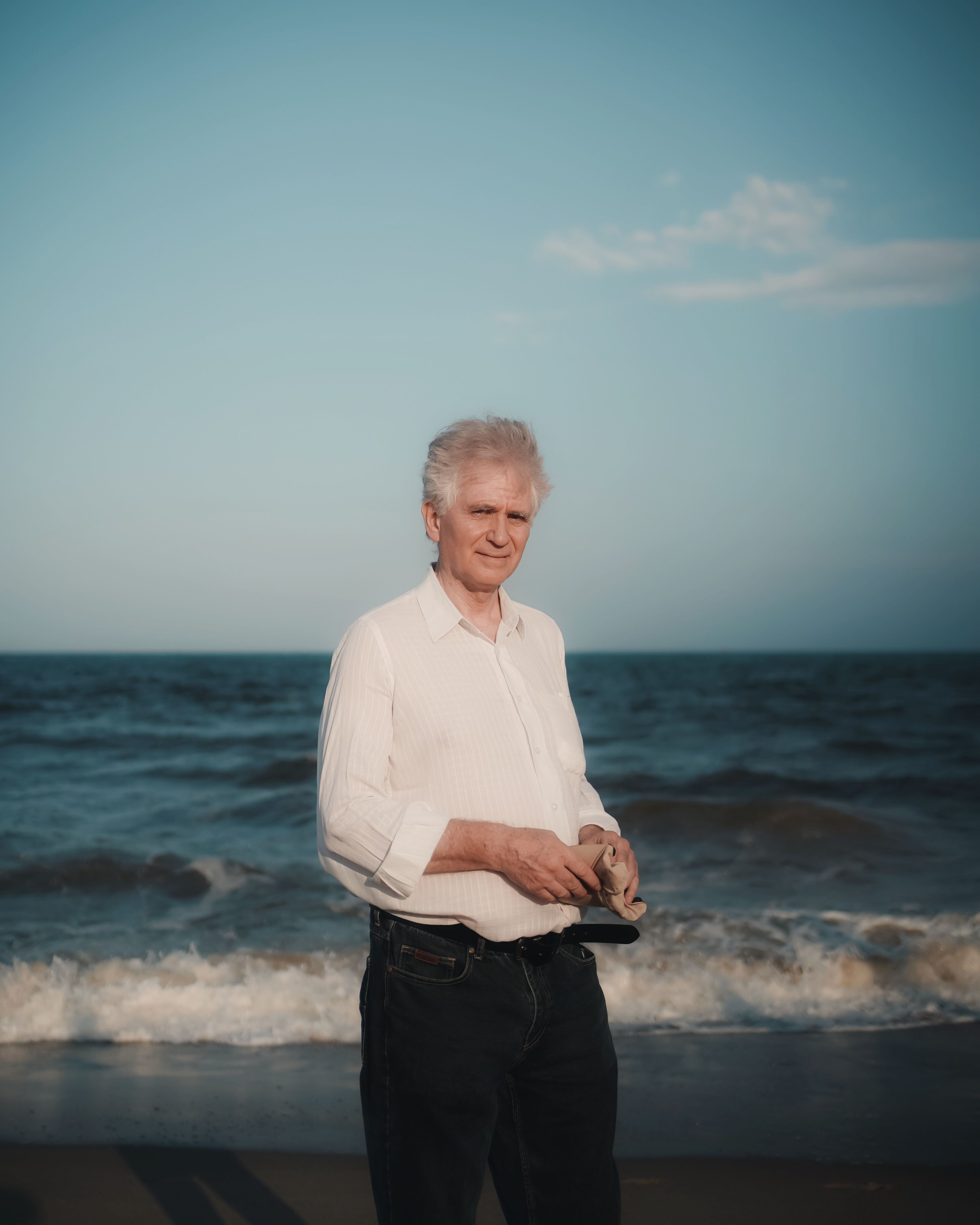 Elegant senior man wearing a white shirt stands by the seashore in Puducherry, India.