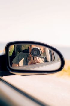 Photographer capturing a moment through car mirror reflection on a sunny day.